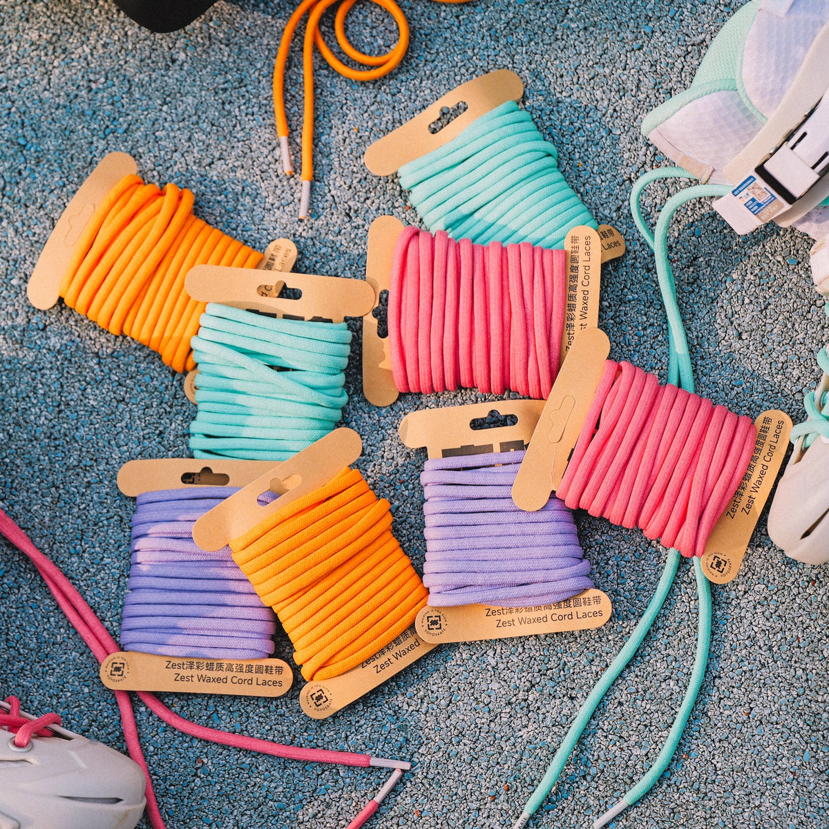 Six pairs of colorful inline skate laces in orange, mint green, pink, and purple, displayed on a blue carpet alongside white inline skates.