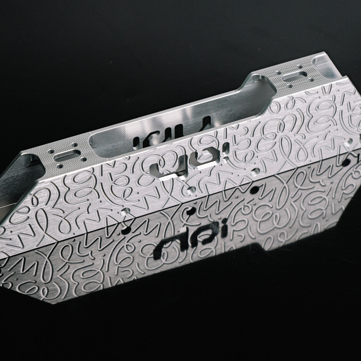 A brushed aluminum metal frame component with intricate laser-cut patterns and the 'nai' brand logo, displayed on a reflective black surface.