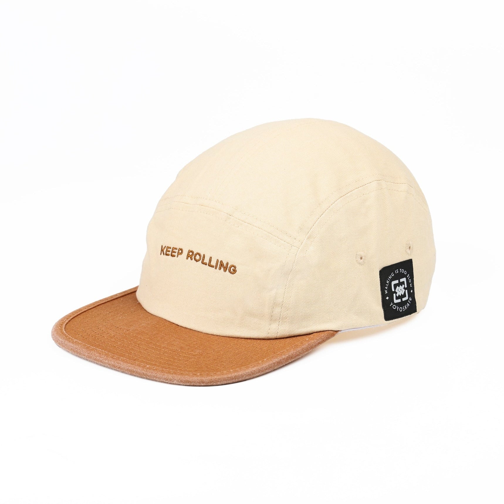 A beige 5-panel camp cap with a brown visor, featuring 'KEEP ROLLING' embroidered on the front and a small black brand patch on the side, set against a plain white background.