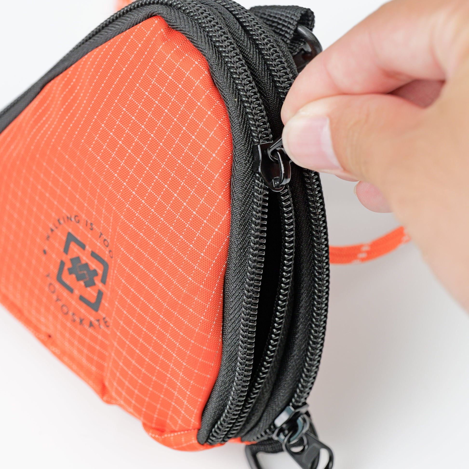 An orange and black zippered pouch with a hand pulling the zipper tab, shown on a clean white background.