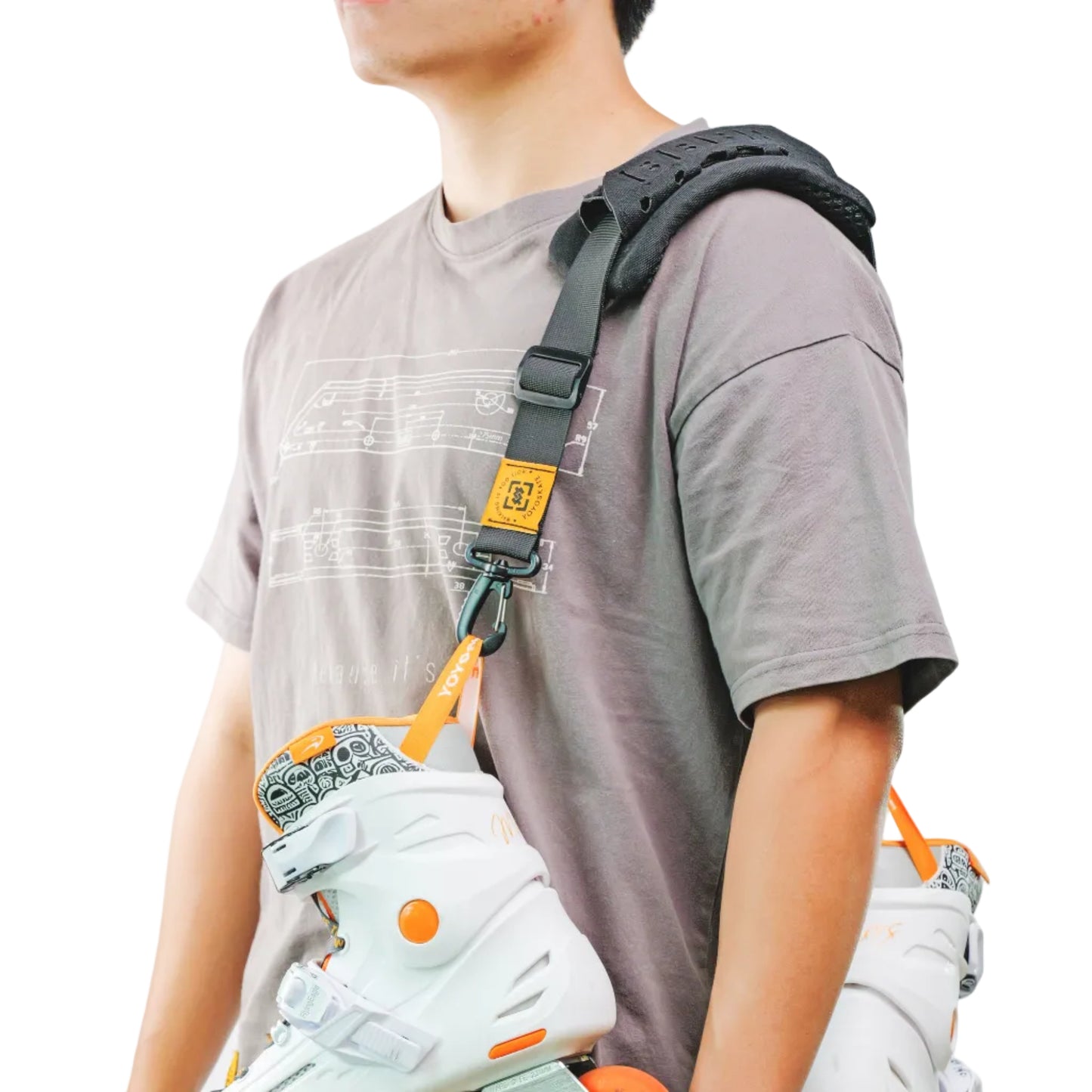 A person models a black shoulder-mounted inline skate harness system holding two white inline skates with bright orange wheels. It's a adjustable shoulder sling for skates.