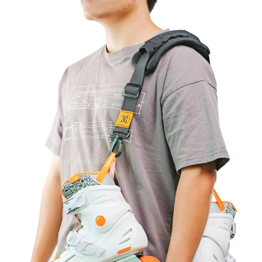 A person models a black shoulder-mounted inline skate harness system holding two white inline skates with bright orange wheels. It's a adjustable shoulder sling for skates.