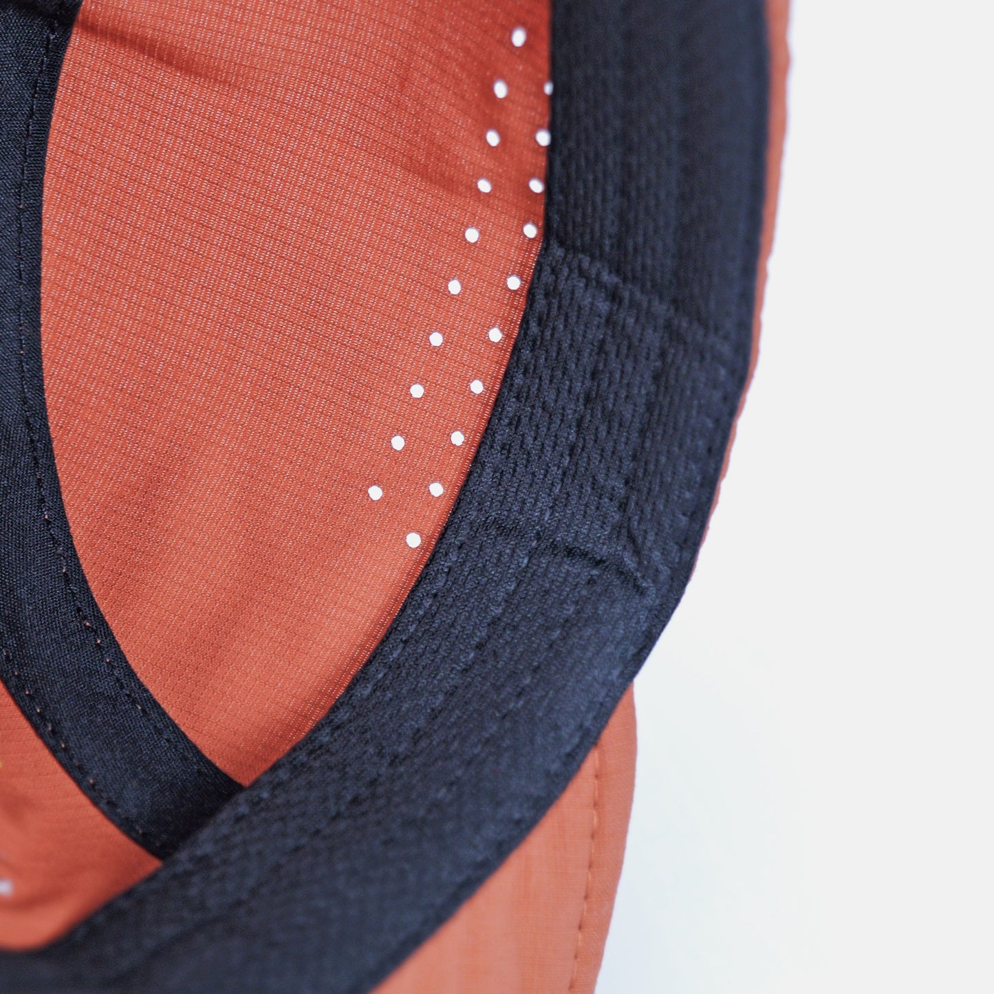 Close-up detail of a baseball cap showing the orange fabric crown, black stitched edge, and white reflective stitching on a white background.