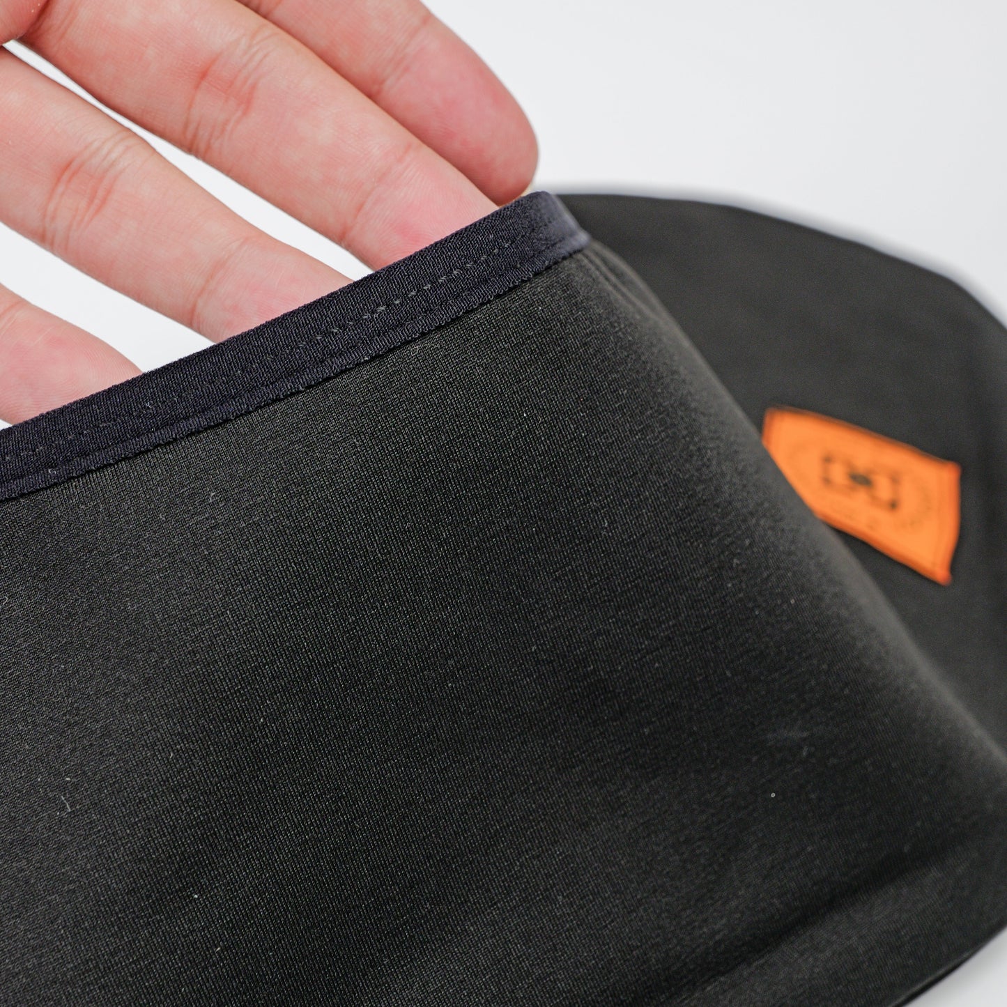 Close-up of a black fabric wheel coverwith a dark navy trim, held by a hand. A small orange brand patch of YOYOSKATE