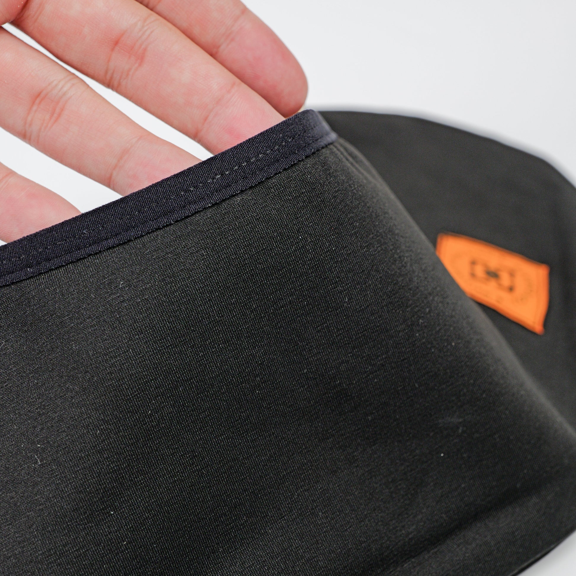 Close-up of a black fabric wheel coverwith a dark navy trim, held by a hand. A small orange brand patch of YOYOSKATE