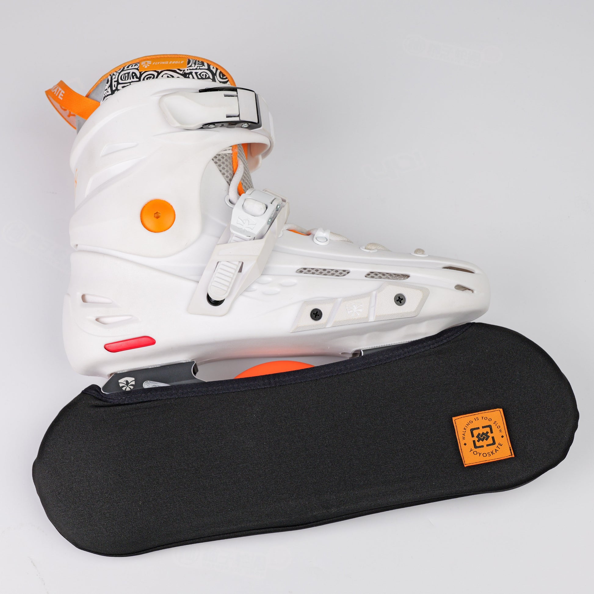 A white inline skate boot with orange accents resting on a black protective wheel cover against a light gray background.