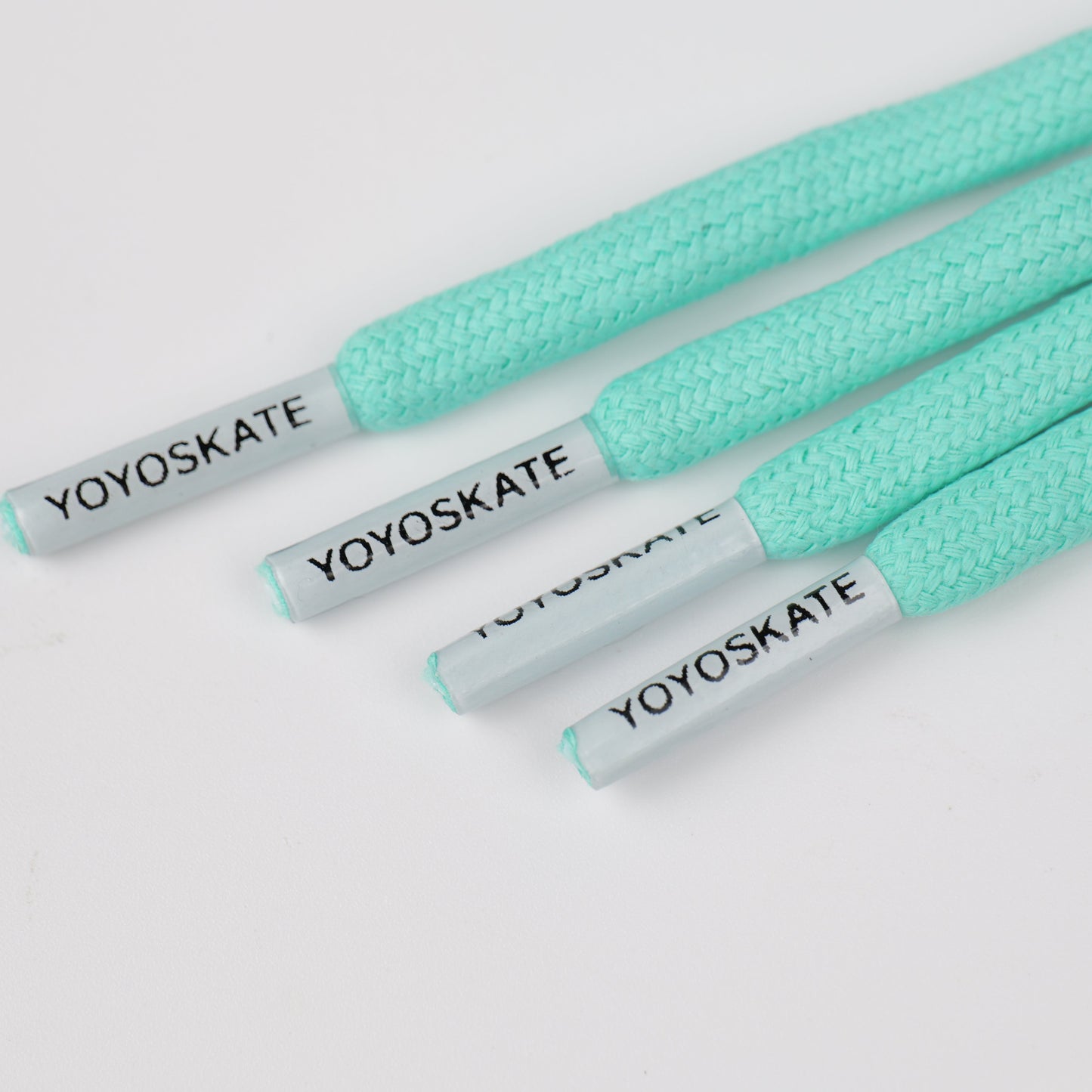 Four mint green braided shoelaces with white tips printed with the black YOYOSKATE brand name, arranged diagonally on a white background.
