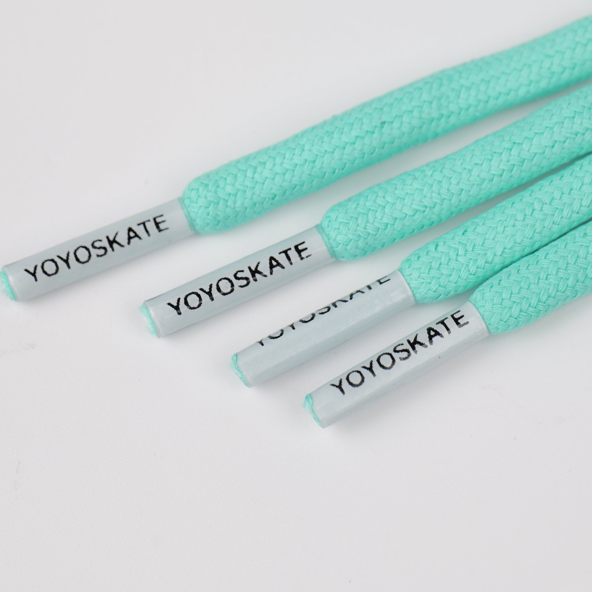 Four mint green braided shoelaces with white tips printed with the black YOYOSKATE brand name, arranged diagonally on a white background.